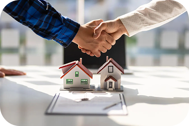 Two people shaking hands above model houses and property documents
